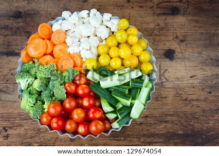 Arrangement of vegetables in a round metal tray as slices, on rustic wooden background
