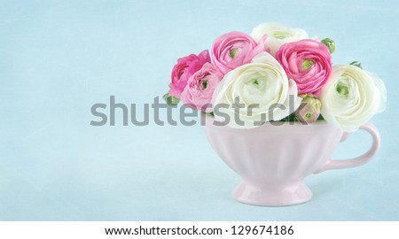 Ranunculus flowers in a pink cup on light blue textured background, with copy space