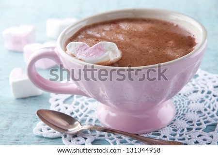 Hot chocolate and a heart shaped marshmallow in a vintage pink cup on light blue wooden background