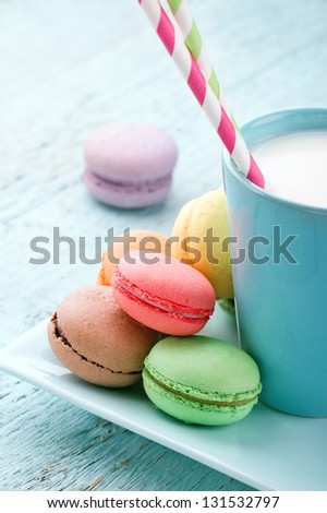 Pastel color macaroons and a cup of milk on vintage light blue wooden background