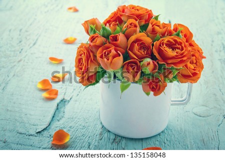 Vintage edited orange roses in a white cup on blue shabby chic wooden background