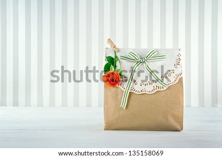 Brown paper gift bag decorated with doily, orange rose and green striped ribbon
