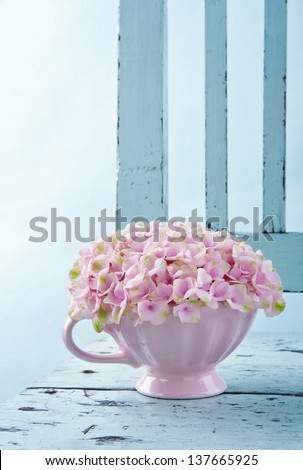 Cup full of pink hydrangea flowers on blue old shabby chic vintage chair
