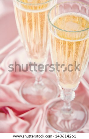 Two glasses of champange or sparkling wine on pink satin background