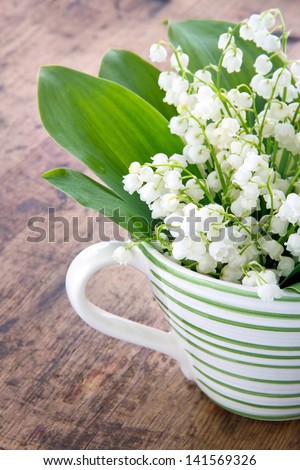 Bouquet of lily of the valley spring flowers in a green striped cup on wooden rustic vintage background