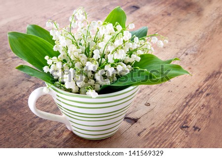 Bouquet of lily of the valley spring flowers in a green striped cup on wooden rustic vintage background