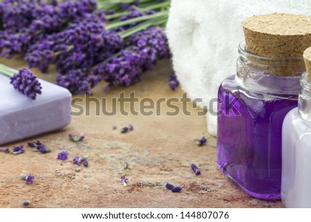 Lavender spa cosmetic and wellness products - white towel, bottles and bar of soap and lotion and bouquet of fresh purple flowers on brown rustic background