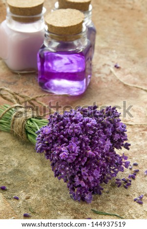 Lavender spa cosmetic and wellness products - bottles of soap and lotion and bouquet of fresh purple flowers on brown rustic background