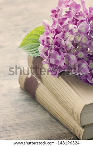 Old books with romantic pink flowers on wooden background, vintage editing