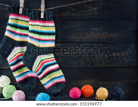 Pair of colorful striped woolen socks hanging on clothesline on dark wooden vintage background with multicolored balls of yarn and room for copy space - knitting concept