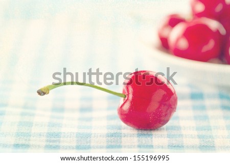 Red cherries on shabby chic blue background with selective focus and vintage creamy textured editing