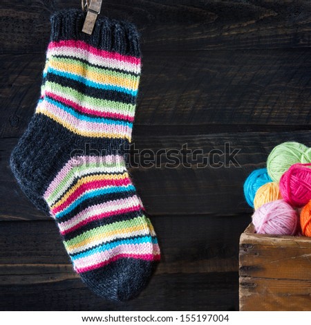 Pair of colorful striped woolen socks hanging on clothesline on dark wooden vintage background with multicolored balls of yarn and room for copy space