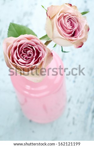 Pink roses in a glass bottle on light blue wooden vintage background
