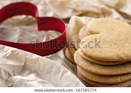 Red heart shaped cookie cutter and a pile of brown homemade Christmas gingerbread cookies