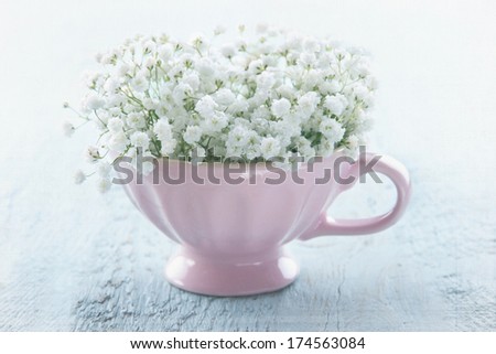 White baby\'s breath flowers in a pink cup on light blue wooden vintage background