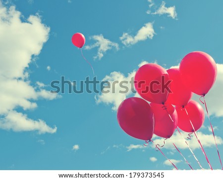 Bunch of red balloons on a blue sky with one balloon escaping to be individual and free - concept for following one\'s dreams