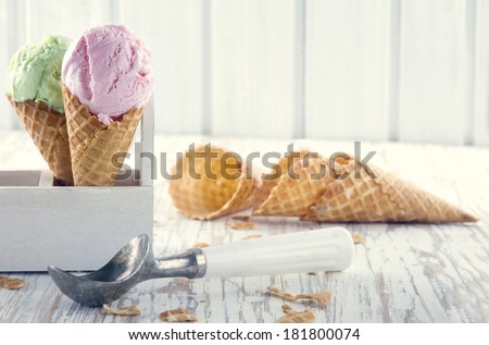 Pink and green ice cream cones with an old metal scoop on wooden rustic background with vintage hazy editing