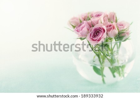 Pink roses in a glass vase filled with water on light blue background with vintage textured editing