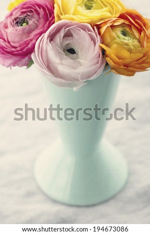 Colorful bouquet of ranunculus flowers in a light blue vase on textured vintage background