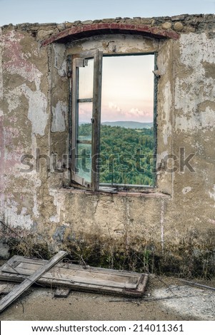 Framed view from an old window in an abandoned stone house to a green Tuscany landscape