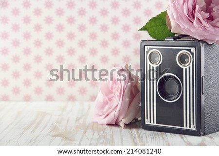 Old classic nostalgic box camera with pink roses on vintage shabby chic background