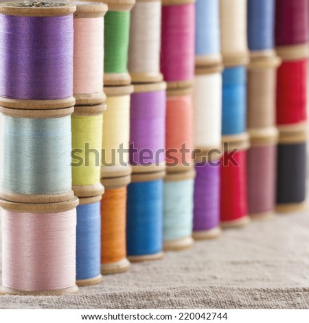 Colorful spools of thread stacked up in piles and lines on linen textile background - sewing concept