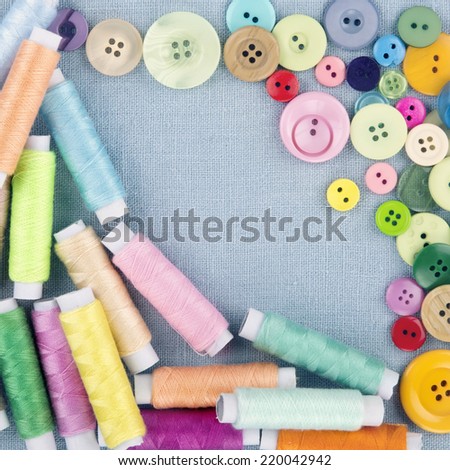 Multicolored buttons and spools of thread on light blue linen textile background - sewing concept