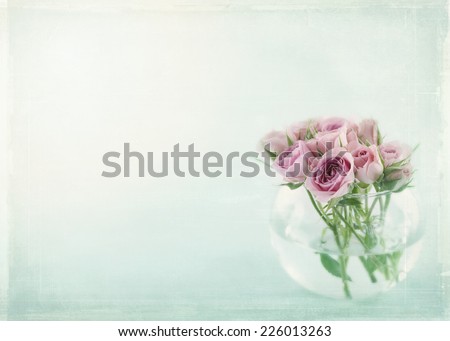 Pink roses in a glass vase filled with water on light blue background with vintage textured editing