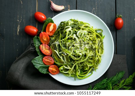 Zucchini raw vegan pasta with avocado dip suace, spinach leaves and cherry tomatoes on plate. On dark background. Vegetarian healthy food