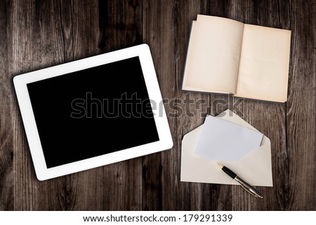 tablet computer and book with letter on old wooden table