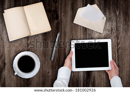 Woman holding hands of a tablet with blank screen on a wooden table coffee book\'s pen