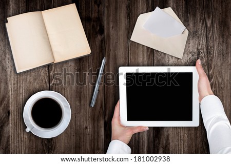Woman holding hands of a tablet with blank screen on a wooden table coffee book's pen