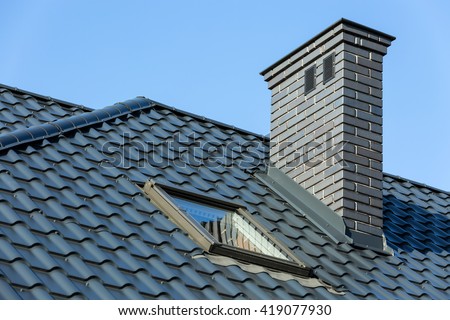 Roof of a detached house with a skylight and chimney against the sky