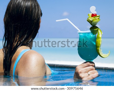 Woman with cocktail relaxing in swimming pool. Focus on glass.