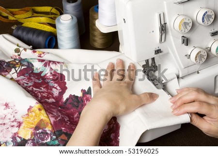 Seamstress sewing on overstitching machine. Sewing items on table.