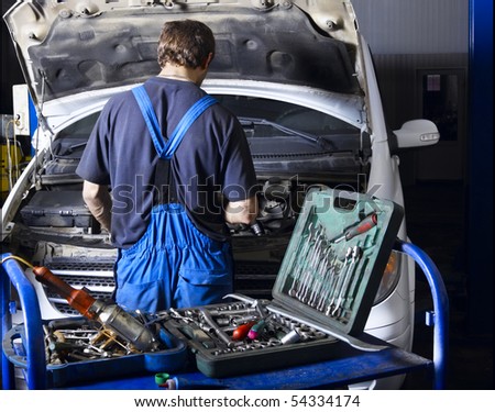 Auto mechanic repairing a car engine. Different work tools on foreground.