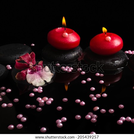 spa concept of red candles, zen stones with drops, orchid cambria flower and pearl beads on reflection water, closeup