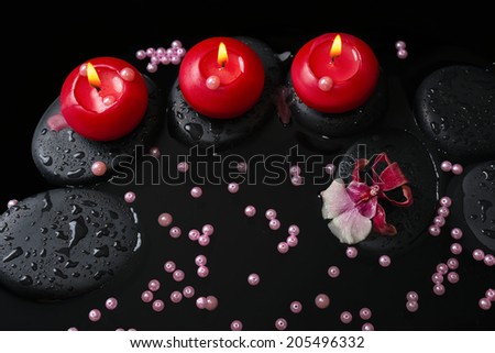 spa concept of red candles on zen stones with drops, orchid cambria flower and pearl beads in reflection water