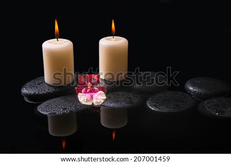 Beautiful spa setting of white and red head orchid (cambria), candles on zen stones with drops, reflection water