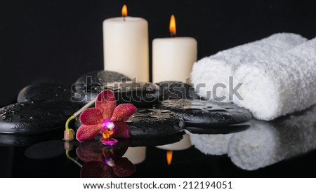 Beautiful spa concept of zen stones with drops, purple orchid (phalaenopsis), candles with reflection on water, white towels