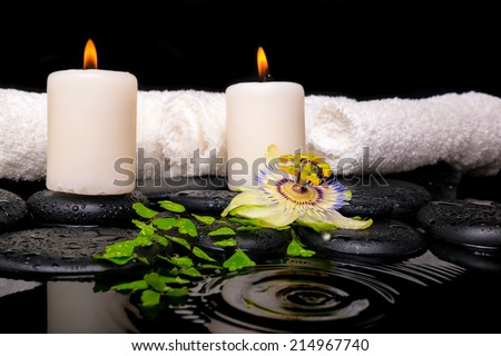 spa setting of passiflora flower, green branch fern, towels and candles on zen stones in ripple reflection water, closeup