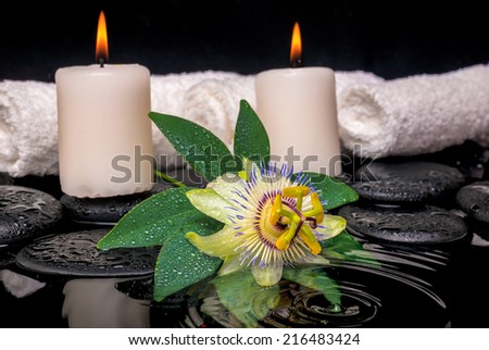 spa concept of passiflora flower, green leaf with drop, towels and candles on zen stones in rippled reflection water