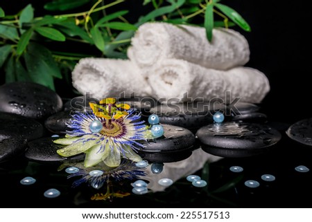 spa setting of passiflora flower, branches, stacked towels, zen basalt stones with drops and pearl beads in reflection water