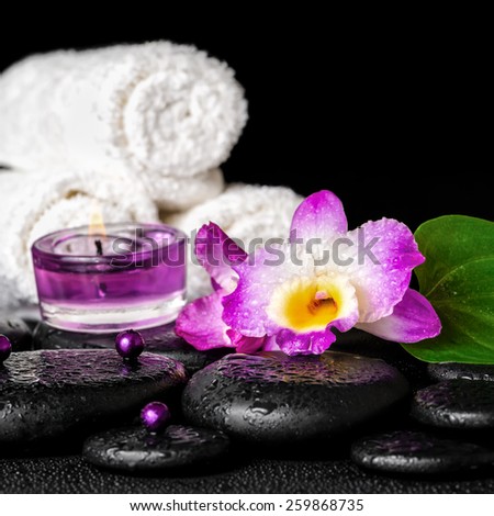 spa concept of orchid flower, zen basalt stones with drops, purple candles, beads and white towels, closeup