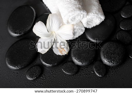 spa concept of white hibiscus flower and towels on zen basalt stone with drops