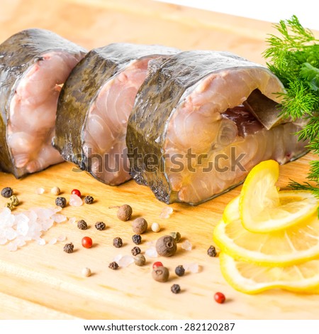 raw sliced steak of sturgeon fish with greens, lemon, different peppers and salt, isolated on white background, closeup