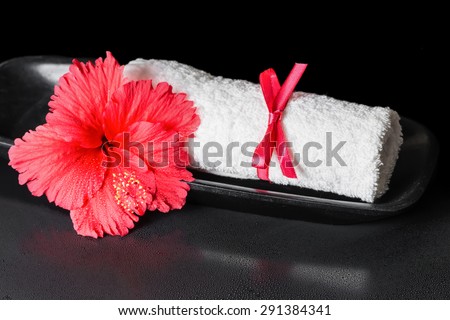 beautiful spa concept of red hibiscus flower with dew and white rolled towel tied with a ribbon