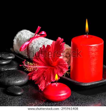 beautiful spa composition  of hibiscus flower with dew, red candles and white rolled towel tied with ribbon on zen stones, closeup