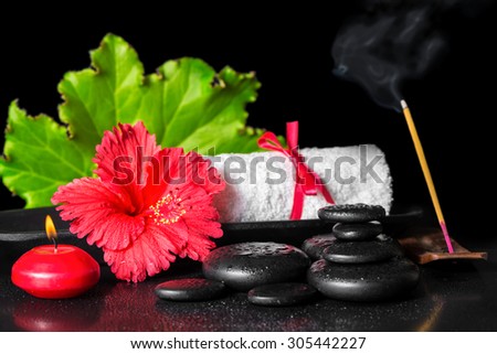 beautiful spa concept of red hibiscus flower with dew, candles, green leaf, scent stick and rolled towel on zen stones