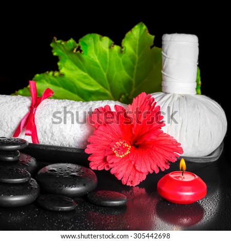 spa concept of red hibiscus flower with dew, candles, leaf, thai herbal compress ball and rolled towel on zen stones, closeup